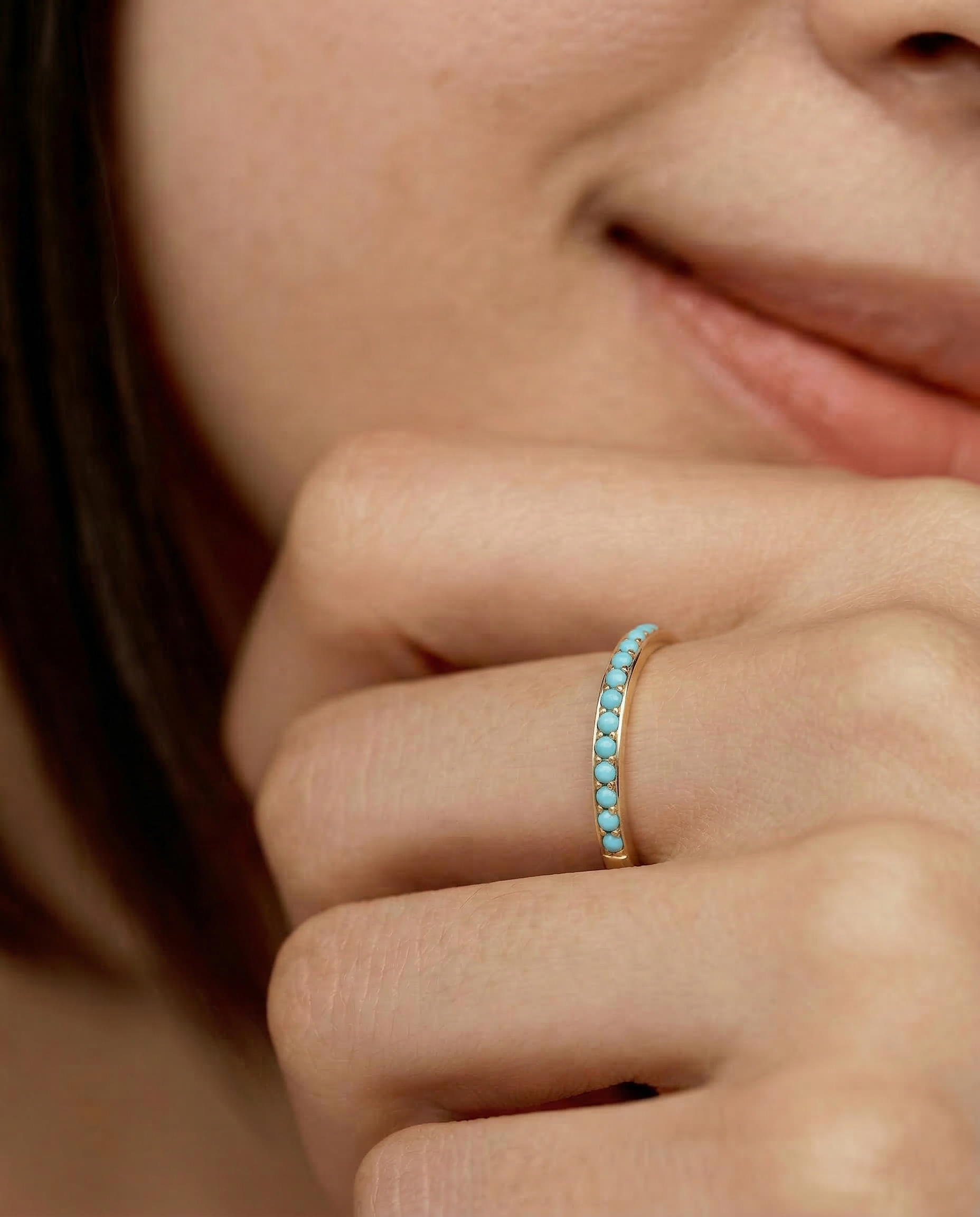 Close-up of a hand wearing a minimalist gold band with a partial pavé of turquoise stones 