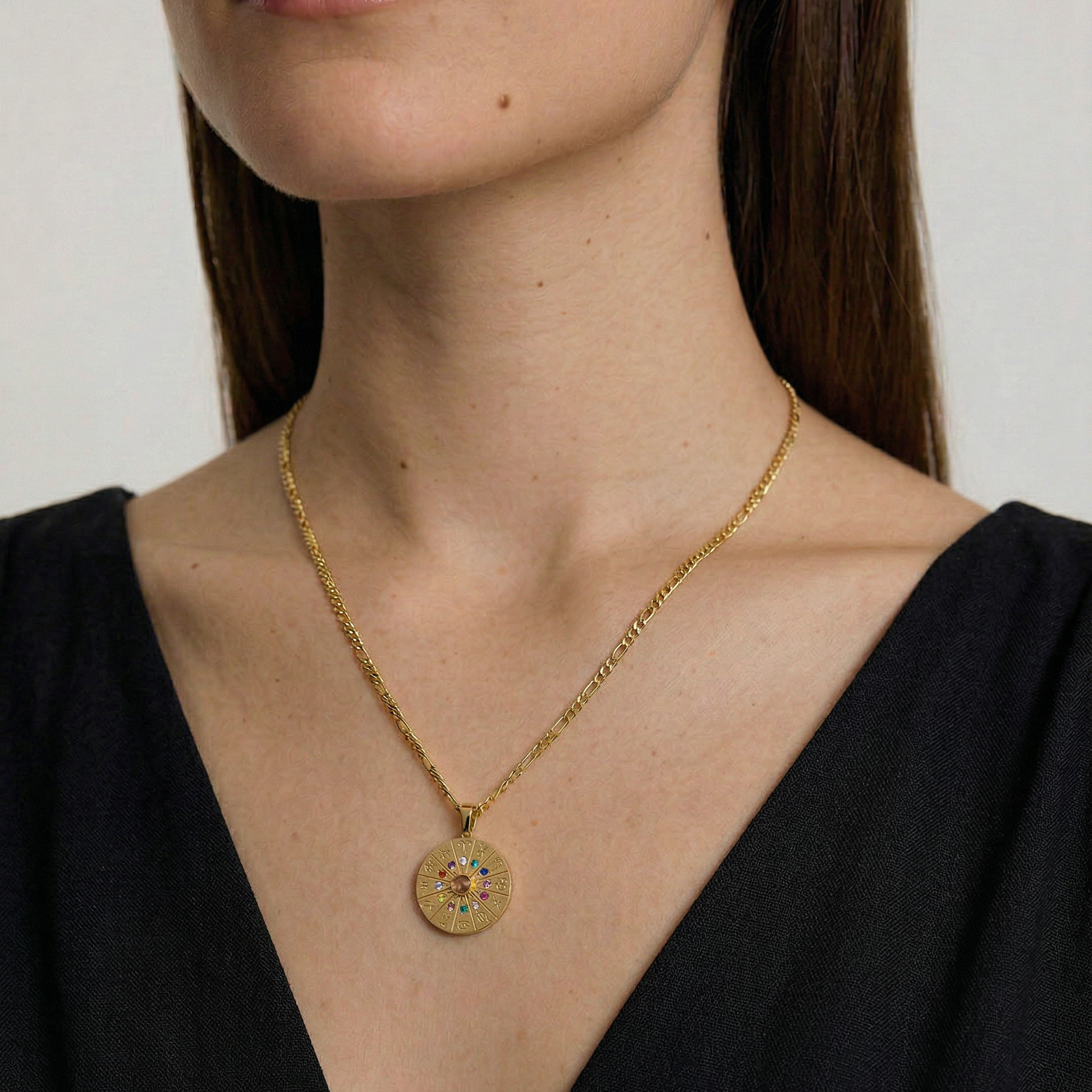 Gold necklace with a round pendant worn by a person against a neutral background
