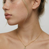 model wearing a gold-plated necklace with a starburst pendant featuring a blue opal in the center