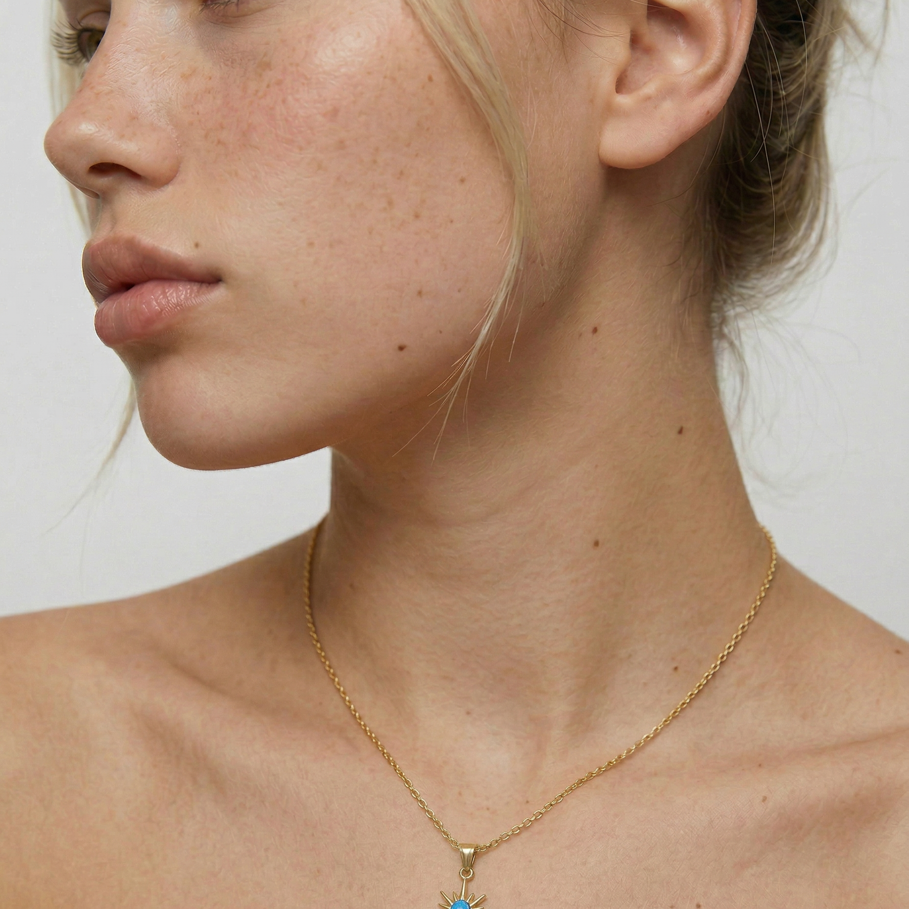 model wearing a gold-plated necklace with a starburst pendant featuring a blue opal in the center