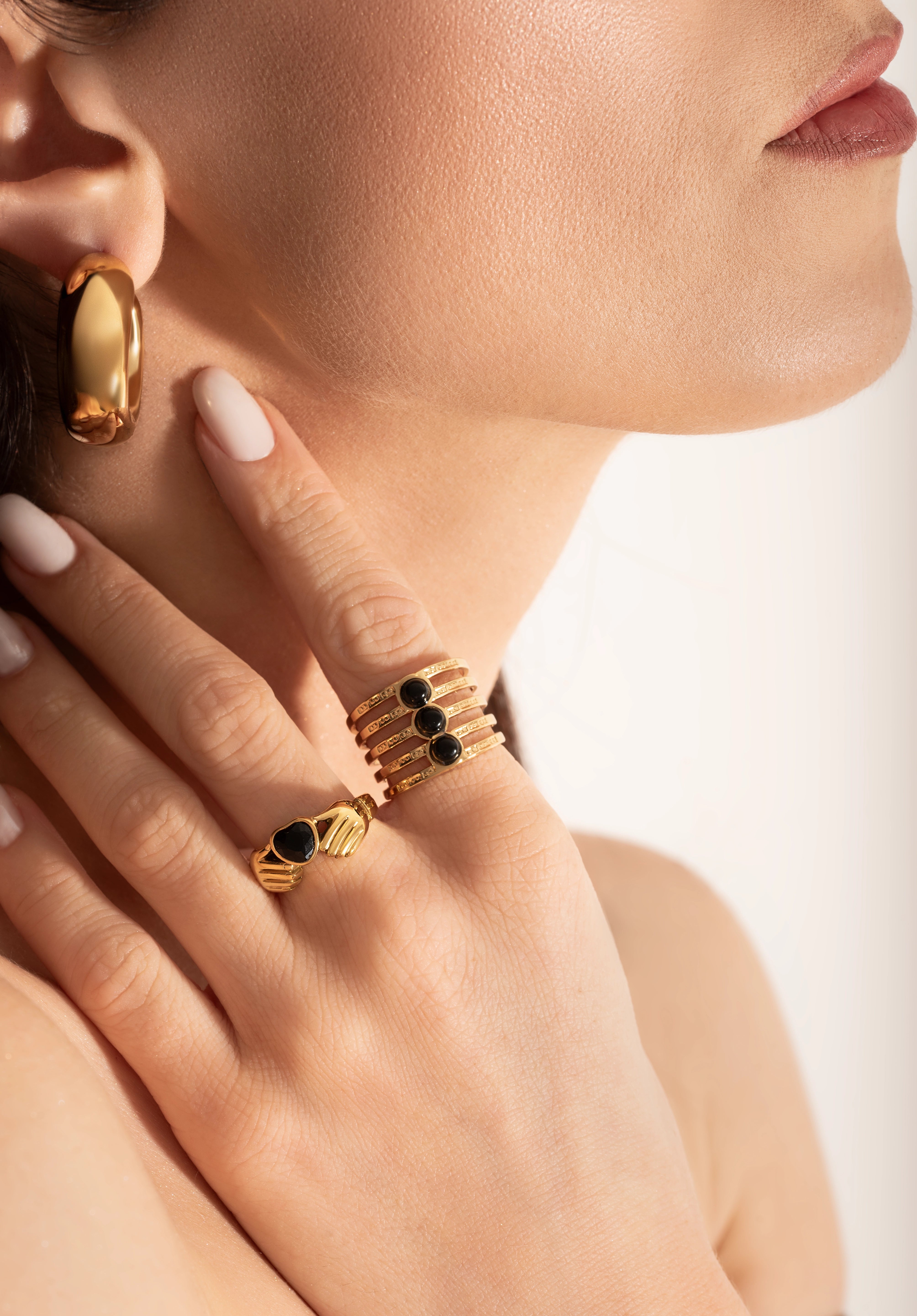 female model wearing 2 gold-plated Claddagh ring with a heart-shaped black gemstone, featuring two hands holding a heart and a crown on top.