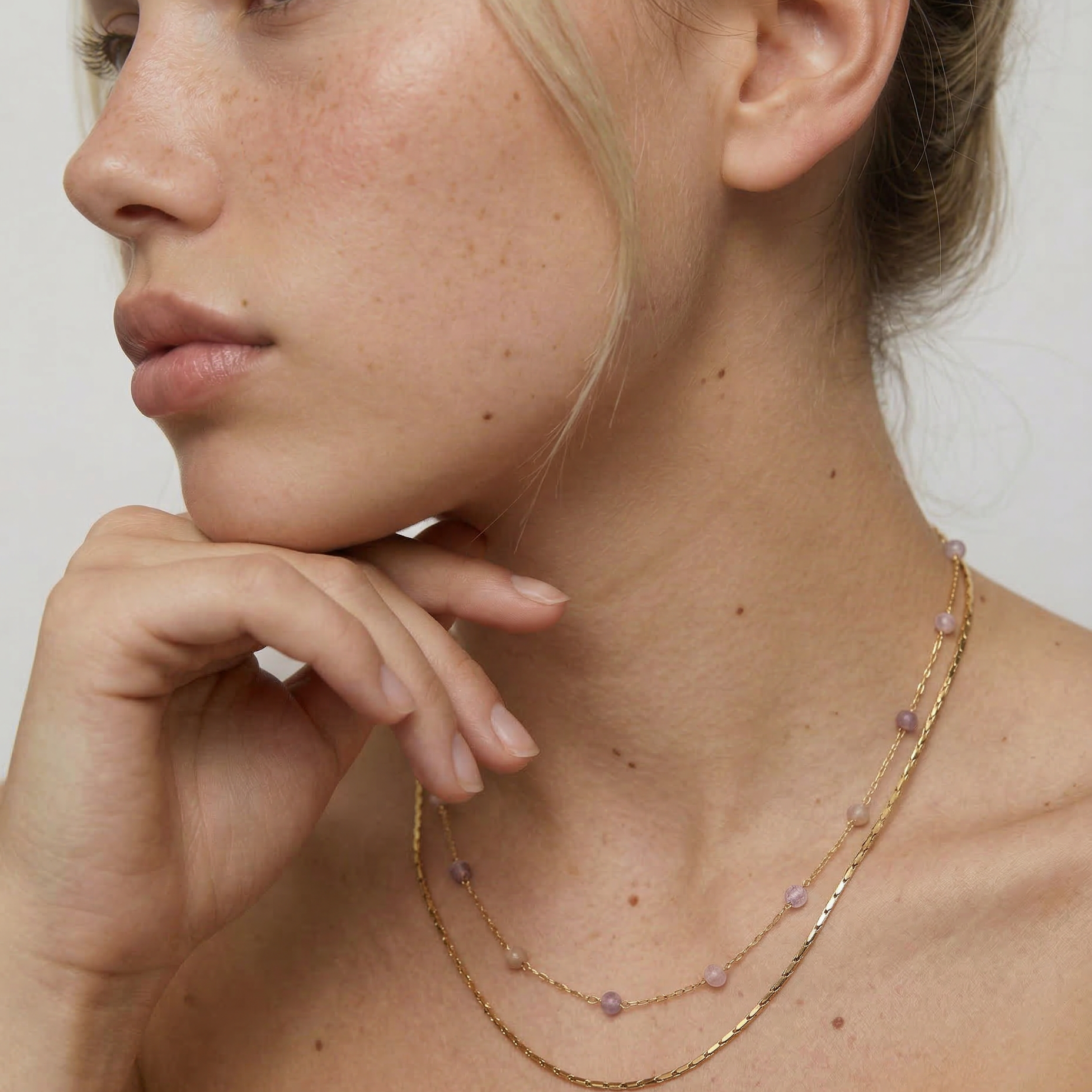 model wearing a two-strand gold-plated necklace with delicate rose quartz beads and a sleek snake chain