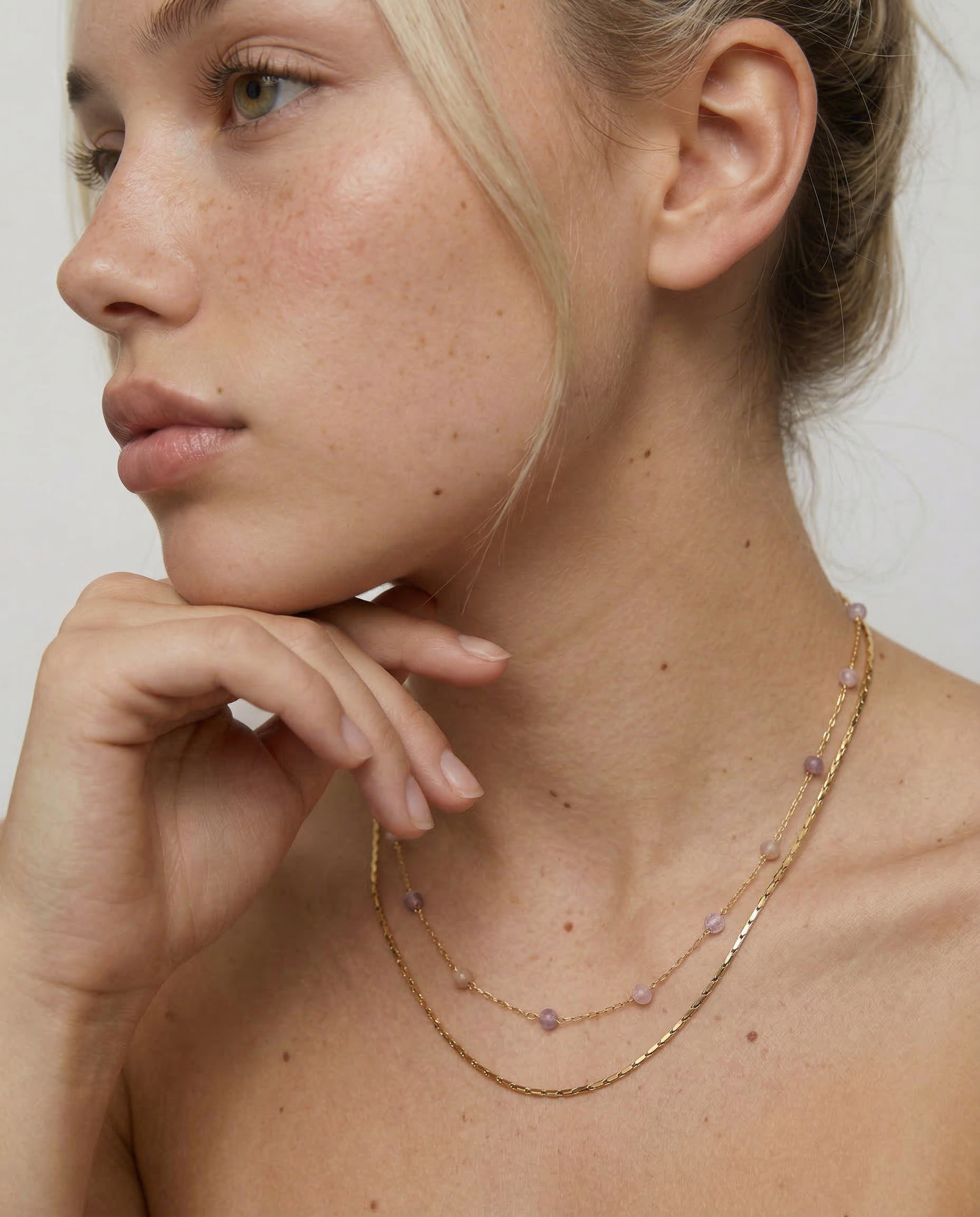 model wearing a two-strand gold-plated necklace with delicate rose quartz beads and a sleek snake chain