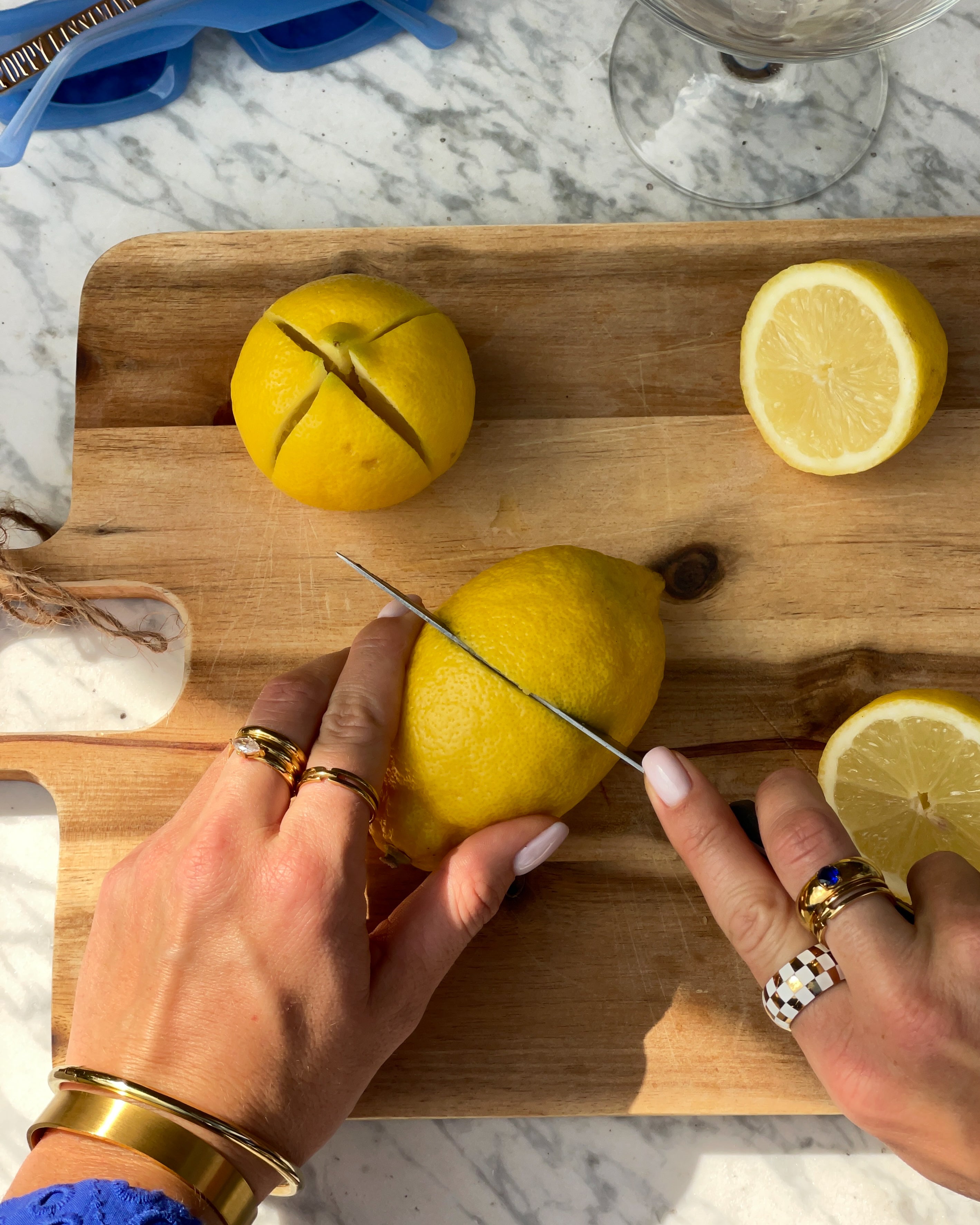Person wearing gold plated jewellery cutting a lemon on a wooden cutting board with a knife.