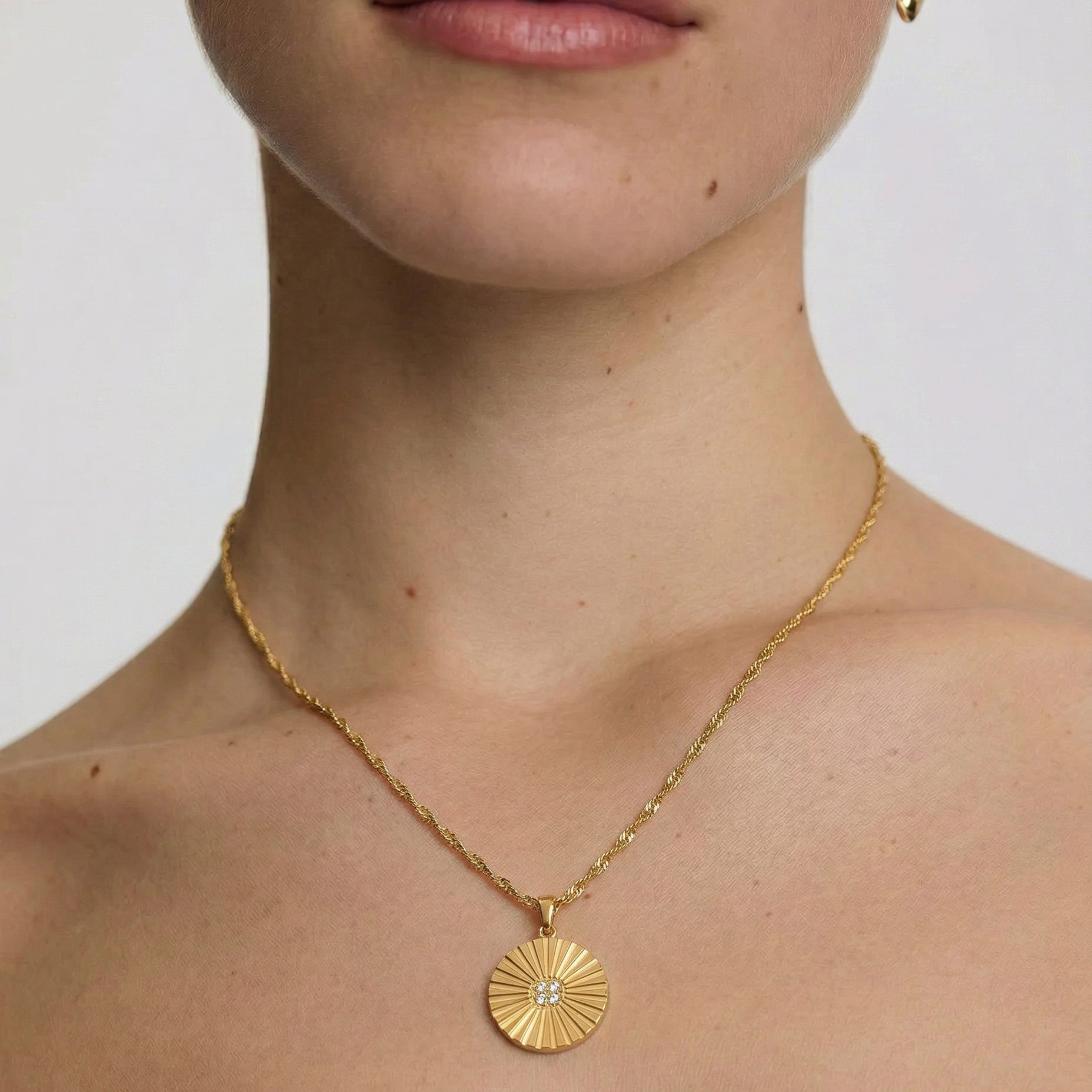 Close-up of a person wearing a gold necklace with a sun-shaped pendant on a plain background
