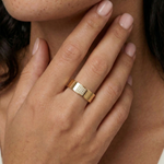 Close-up of a hand wearing a gold ring with a circular design and small stones.