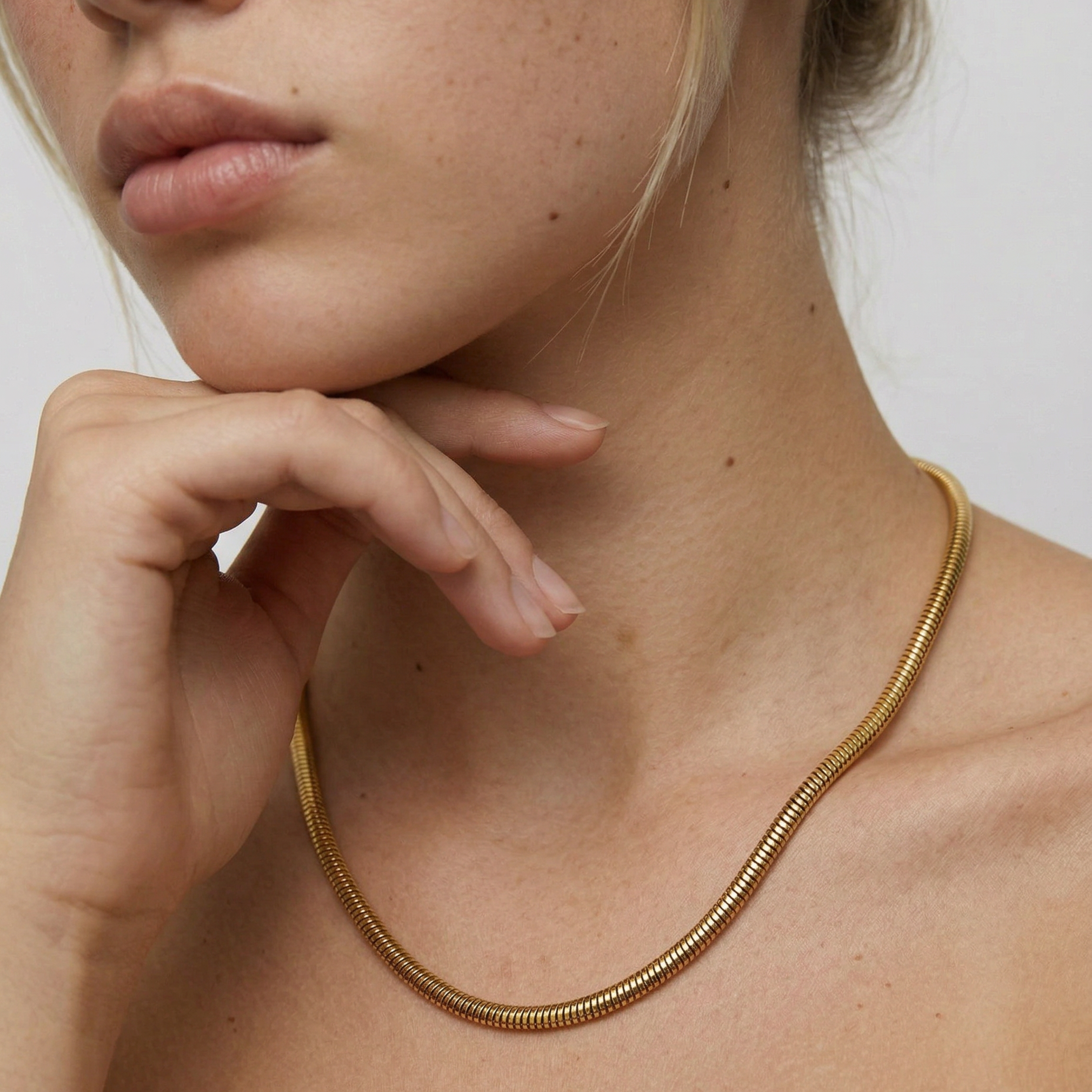 Close-up of a person wearing a gold necklace against a neutral background
