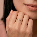 Close-up of a woman's hand wearing a gold ring with a soft focus on her face.