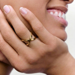 close up of a model wearing a gold-plated ring with two slender bands that intersect creating a modern X-shape design