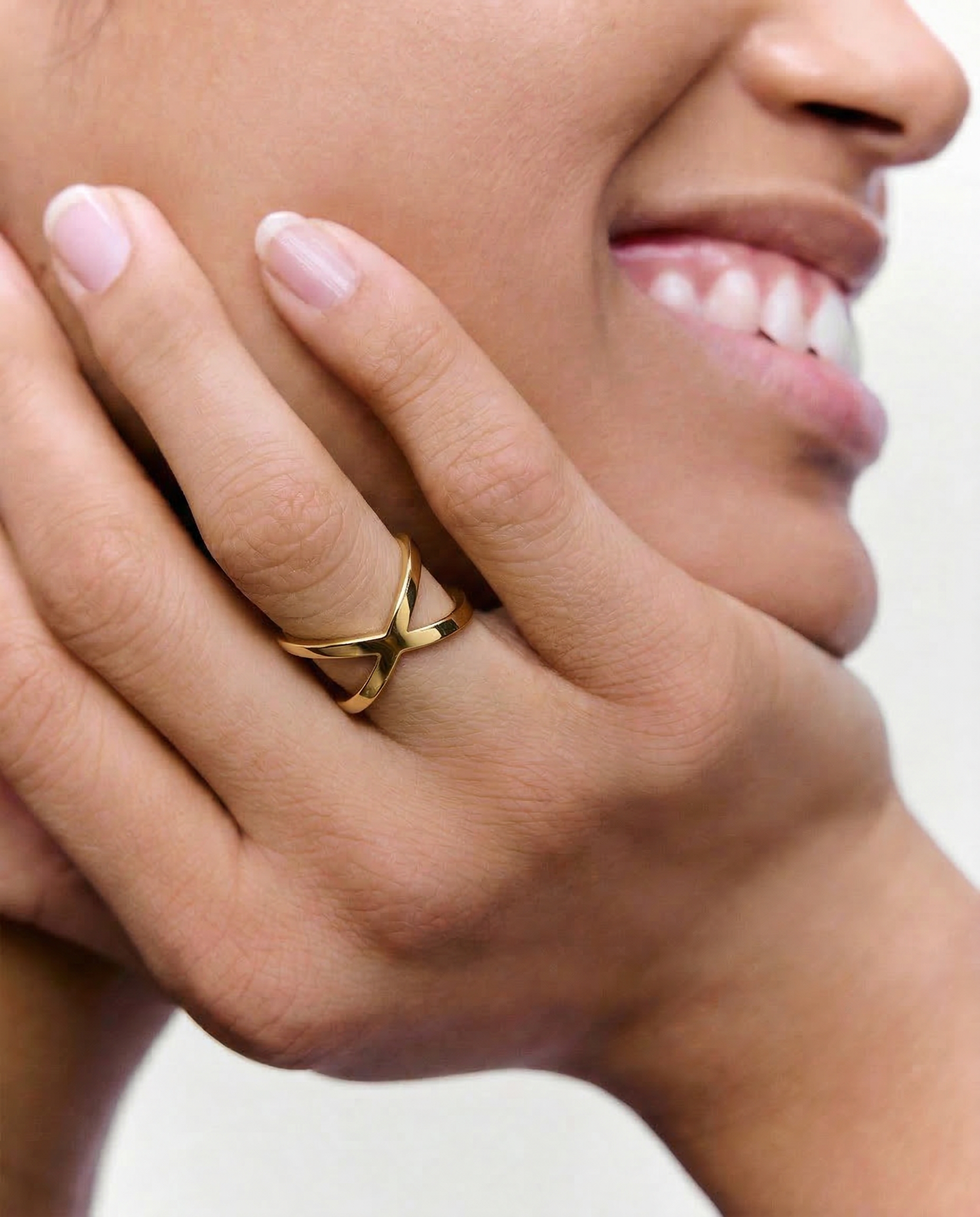 close up of a model wearing a gold-plated ring with two slender bands that intersect creating a modern X-shape design