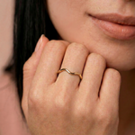Close-up of a hand wearing a gold-plated metal ring with a fluid, asymmetrical wave design