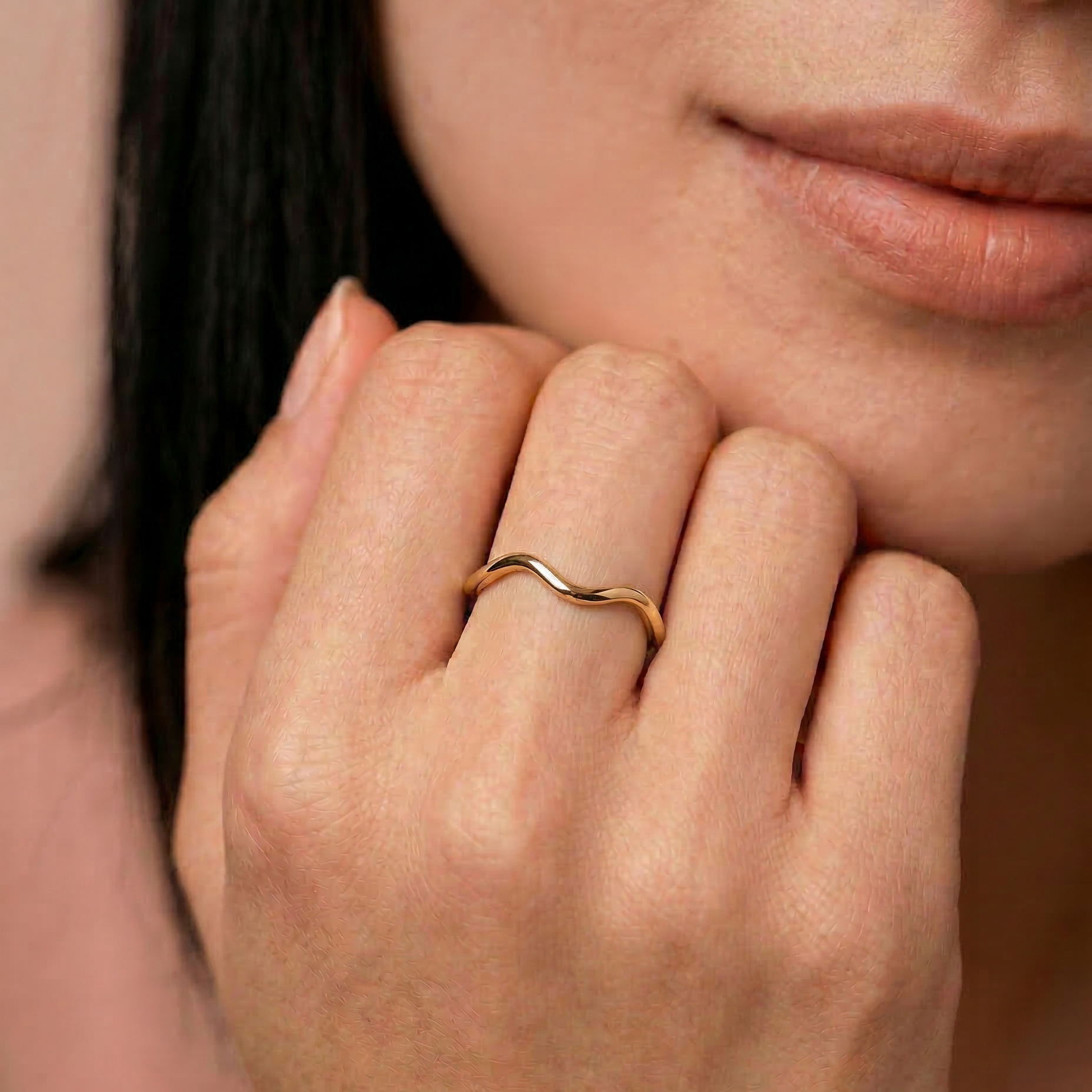 Close-up of a hand wearing a gold-plated metal ring with a fluid, asymmetrical wave design