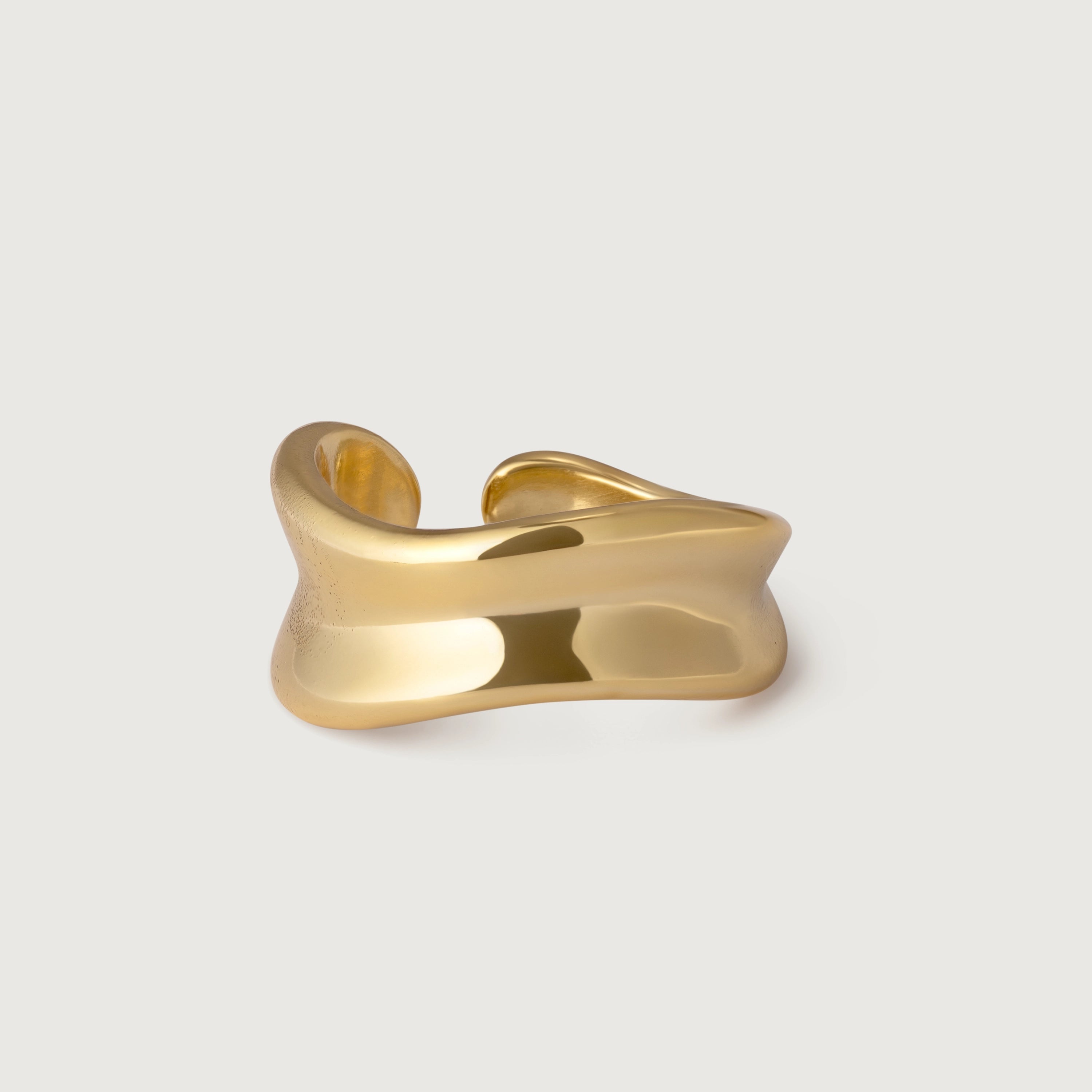 A gold-plated ring with a smooth, organic form that wraps around the finger, featuring gentle curves and hollows.