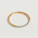A minimalist gold band with a partial pavé of turquoise stones on the top half, displayed against a white background.