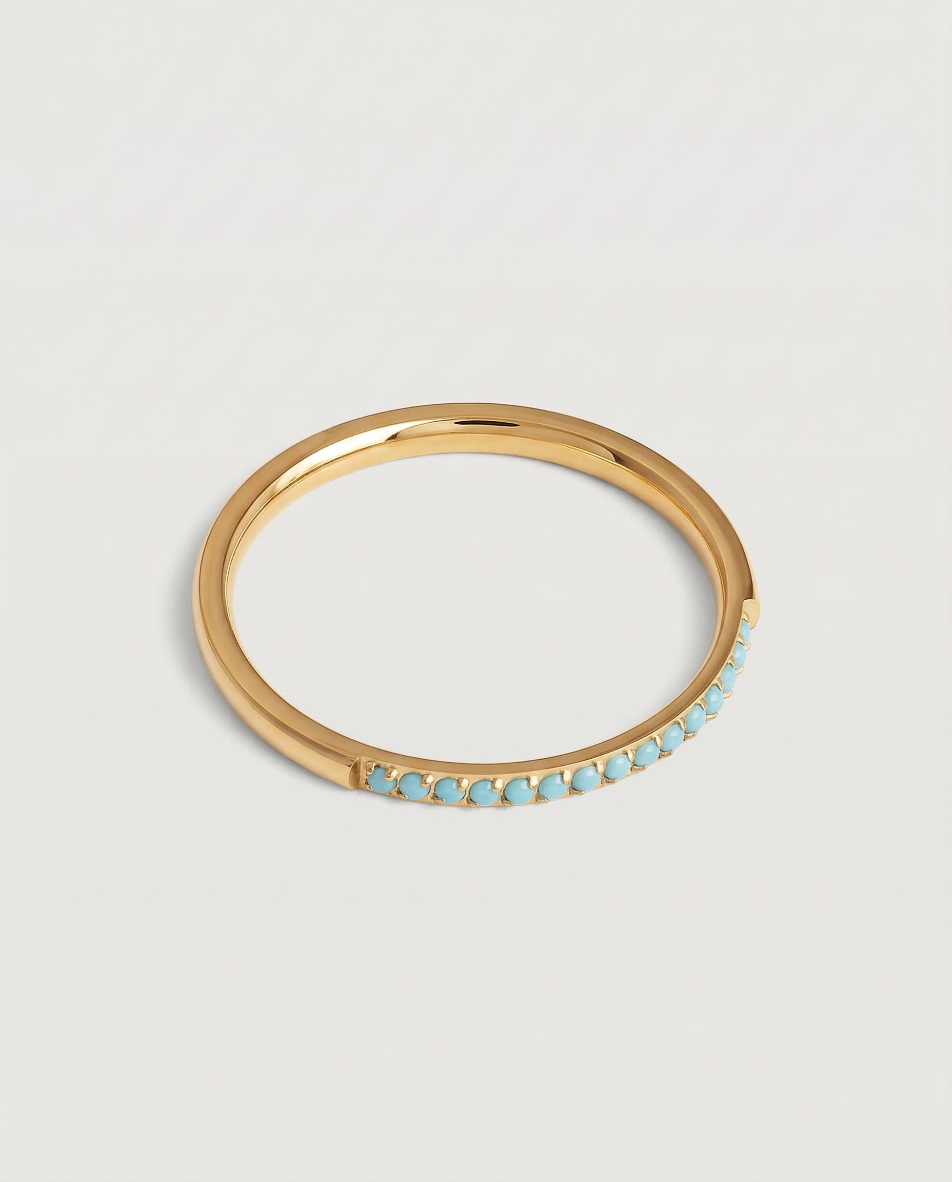 A minimalist gold band with a partial pavé of turquoise stones on the top half, displayed against a white background.