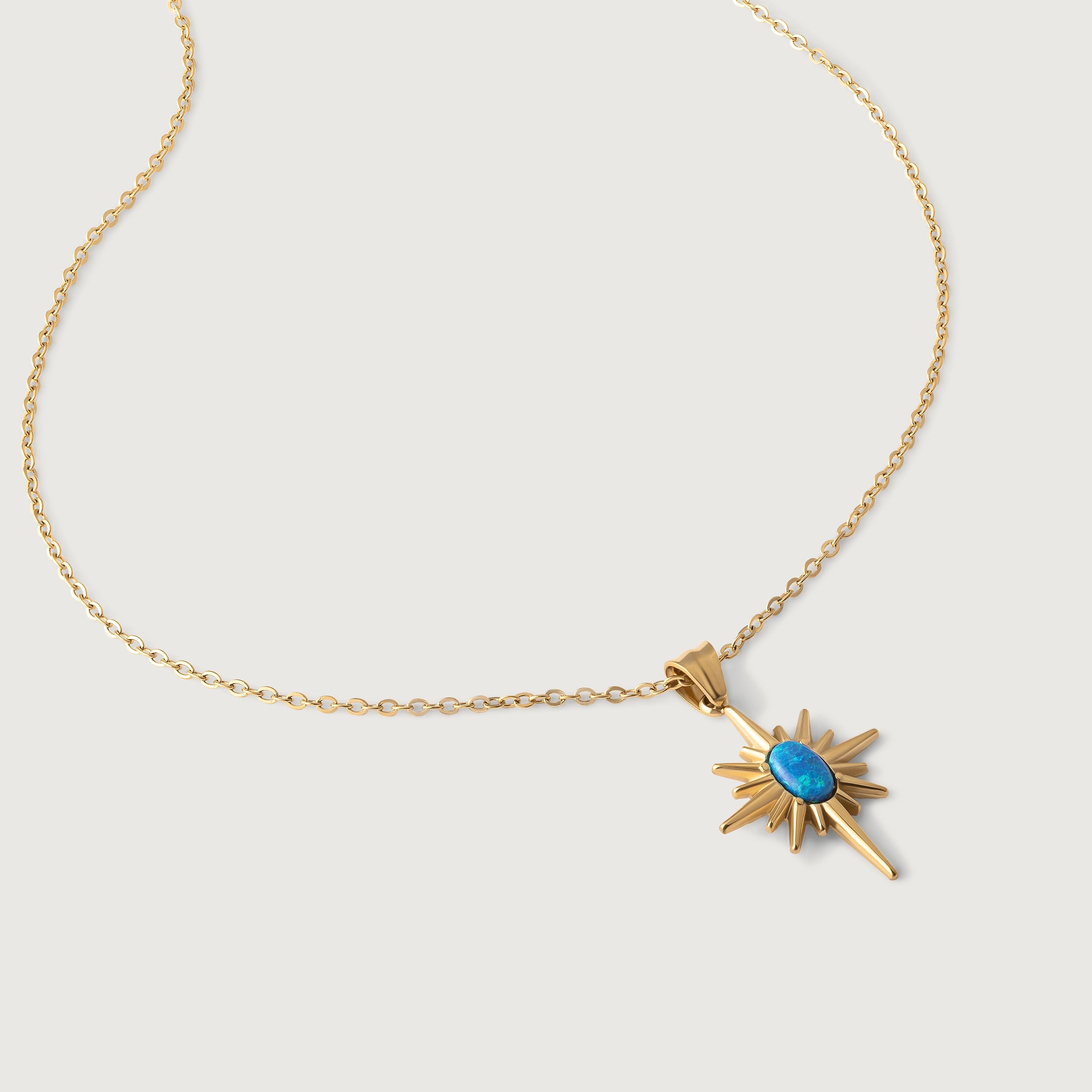 A gold-plated necklace with a starburst pendant featuring a blue opal in the center, suspended on a chain.
