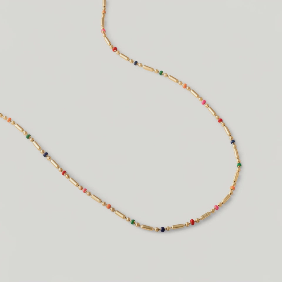 video of a gold-plated necklace with multicolored beads in red, pink, blue, and green, arranged in a alternating pattern between golden bars.