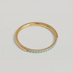 a rotating video of a minimalist gold band with a partial pavé of turquoise stones 