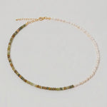 video of a multi gemstone and pearl beaded necklace in gold, with one half strung with imitation pearl rice beads and the other half with faceted mixed quartz beads in green, sage, olive