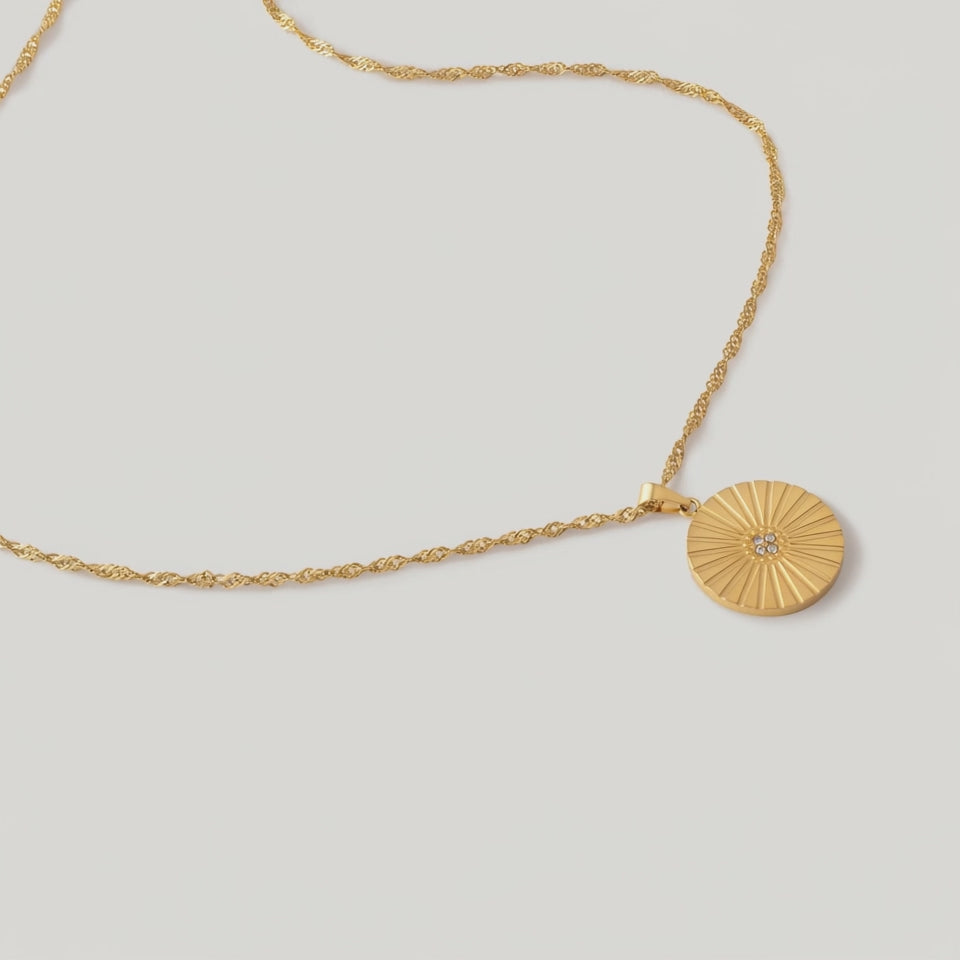 rotating video of a gold-colored necklace with a radially textured medallion pendant hanging from a twisted rope chain.