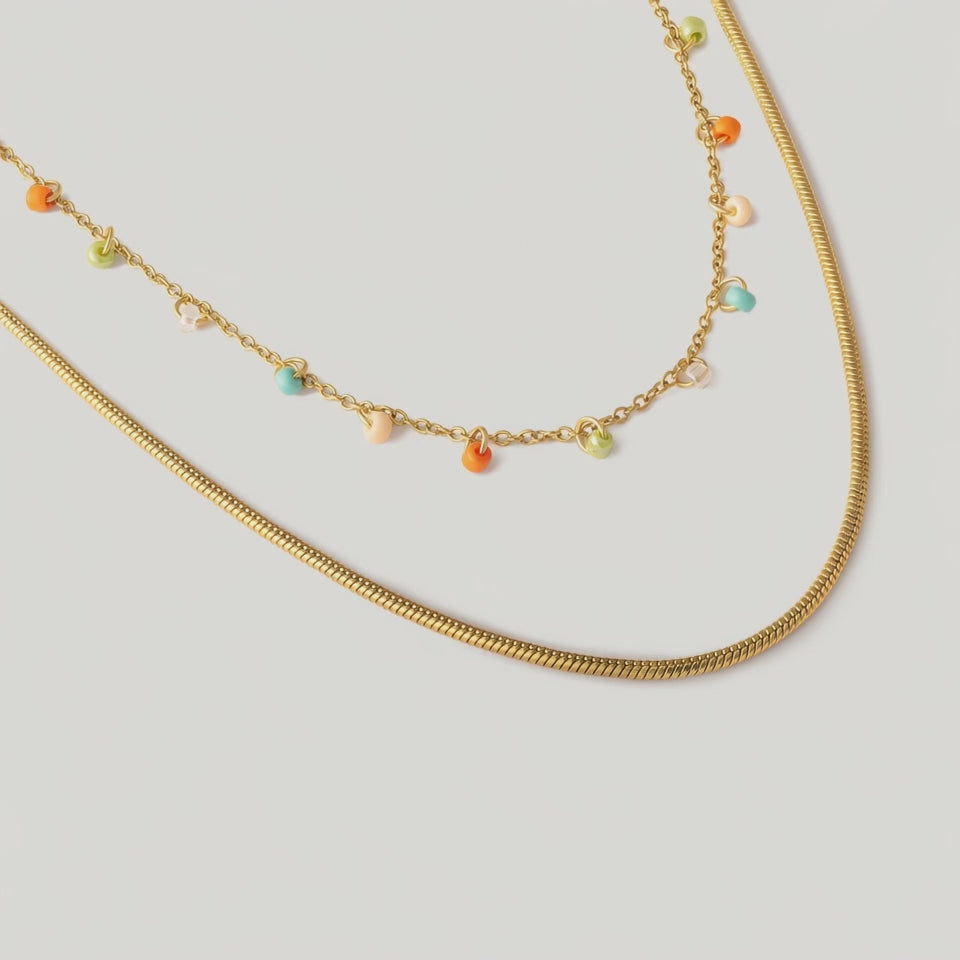video of A double-strand necklace with a gold chain and colorful glass beads in orange, green, and yellow hues, alongside a snake chain.