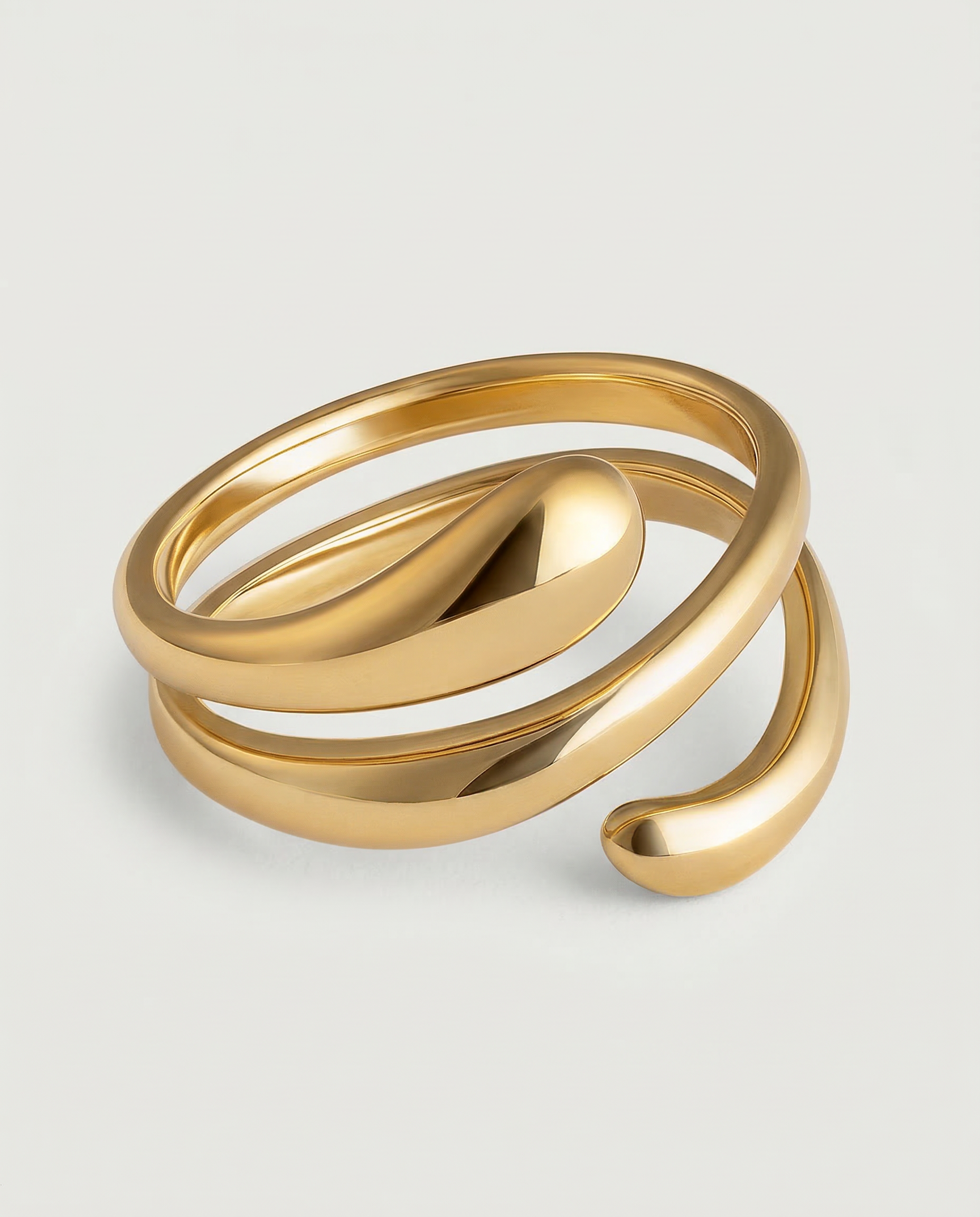 A gold-plated stainless steel ring with an architectural, coiled design, displayed against a white background.