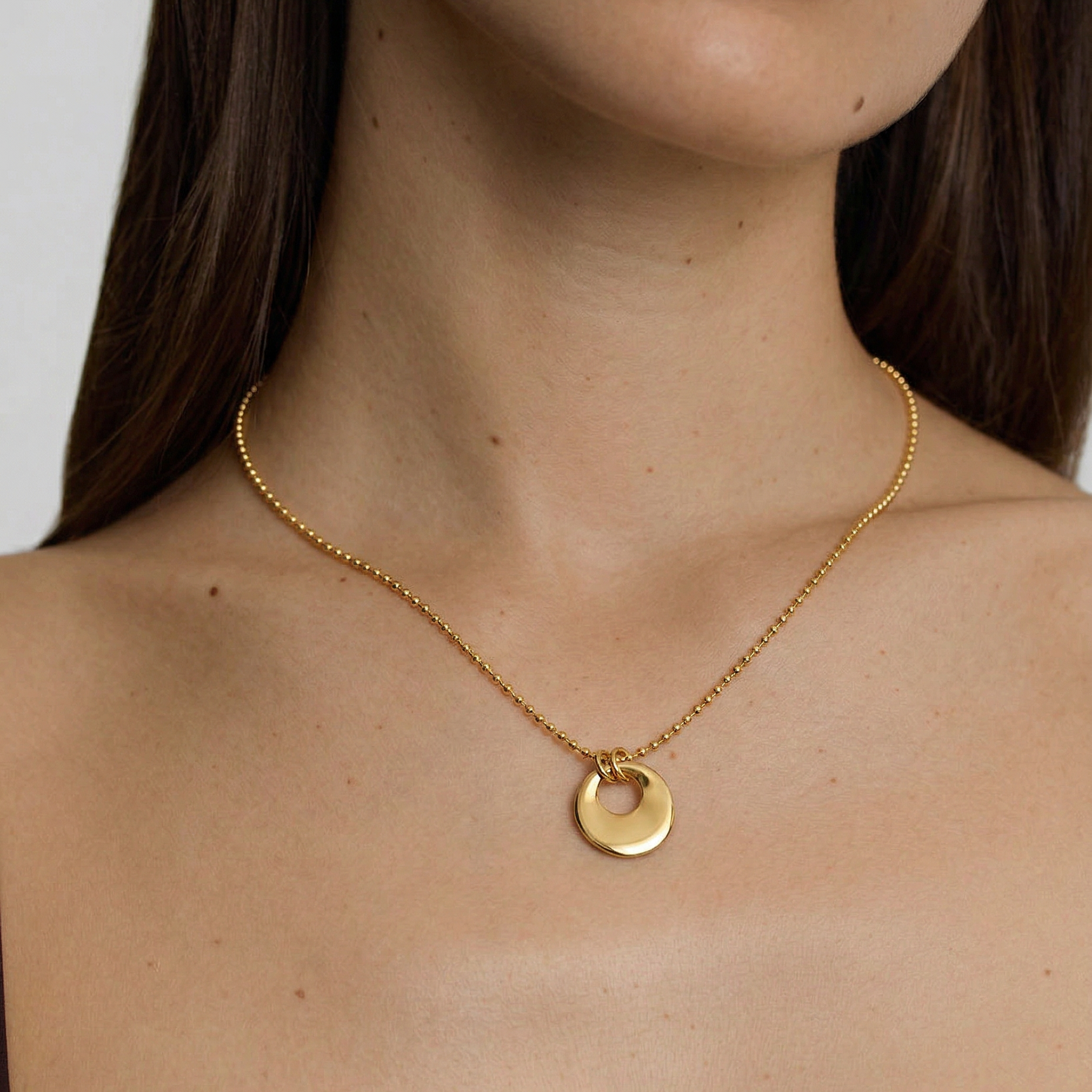 model wearing a gold-plated necklace with a circular charm