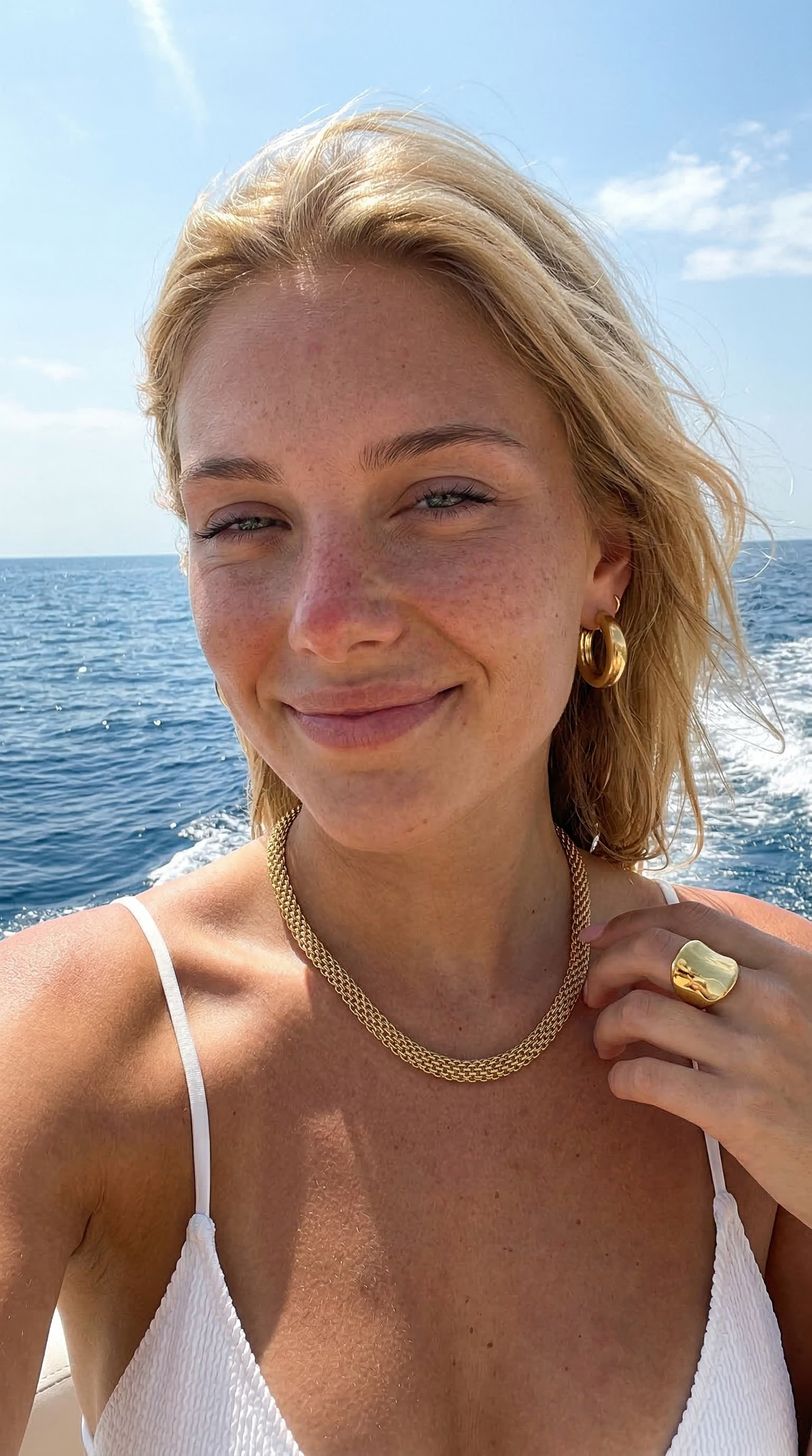 Woman with blonde hair and gold jewelry by the ocean