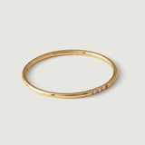 A gold-plated ring with a polished surface and a trio of brilliant cut cubic zirconia stones on one side, displayed against a white background.