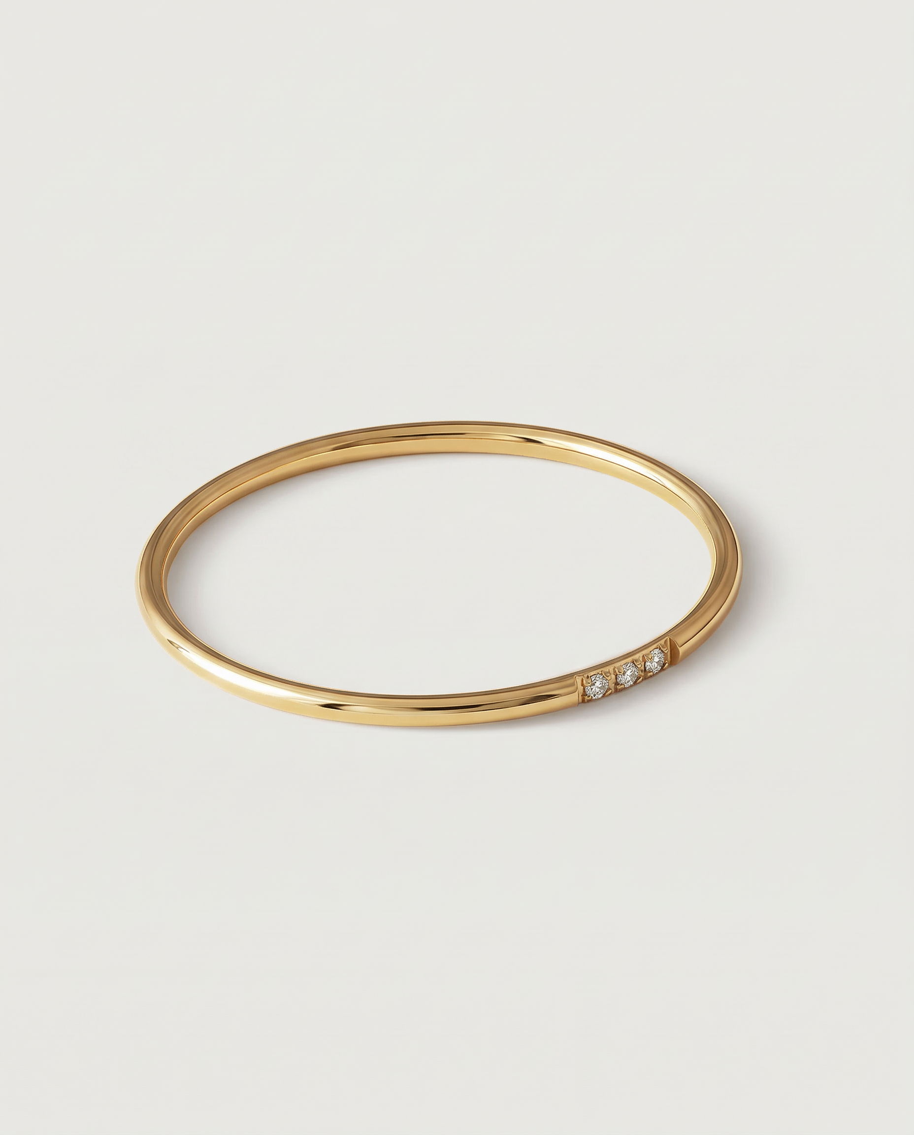 A gold-plated ring with a polished surface and a trio of brilliant cut cubic zirconia stones on one side, displayed against a white background.