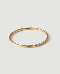 A gold-plated ring with a polished surface and a trio of brilliant cut cubic zirconia stones on one side, displayed against a white background.